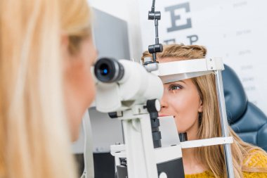 optometrist examining patient through slit lamp in clinic clipart