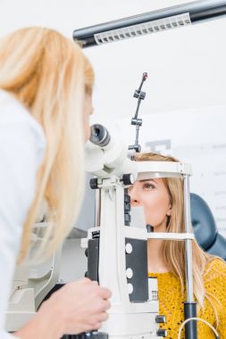 optician examining patient through slit lamp in clinic clipart