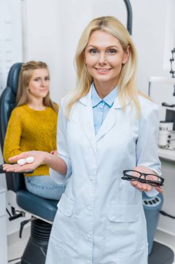 gözlük ve Kontakt lens, arkasında oturan hasta holding beyaz paltolu optometrist