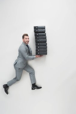 overhead view of young businessman carrying stack of folders isolated on grey