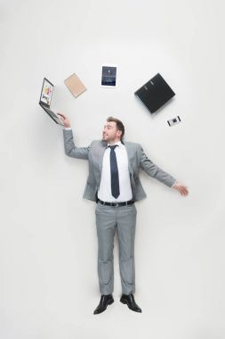 overhead view of businessman with office supplies above head using laptop isolated on grey clipart