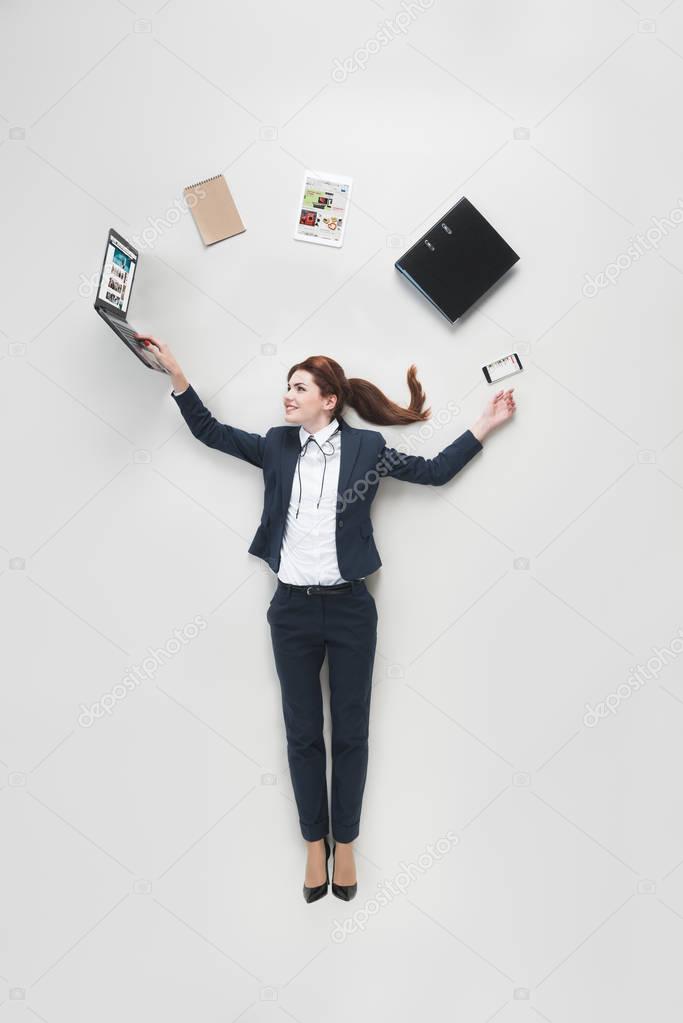 Overhead view of businesswoman with various office supplies using laptop isolated on grey