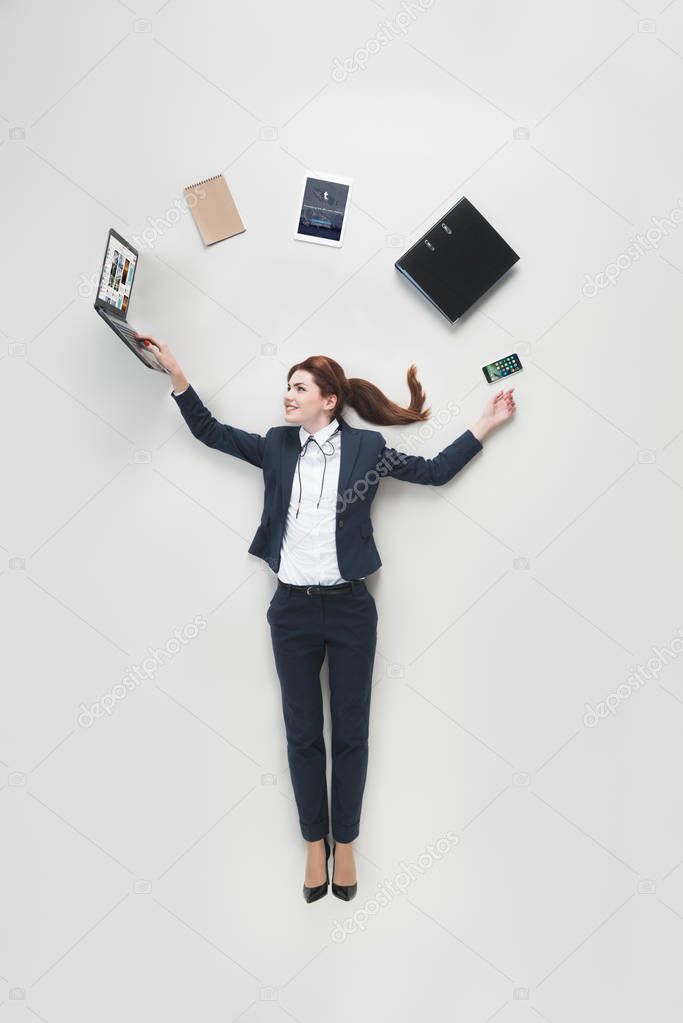 Overhead view of businesswoman with various office supplies using laptop isolated on grey