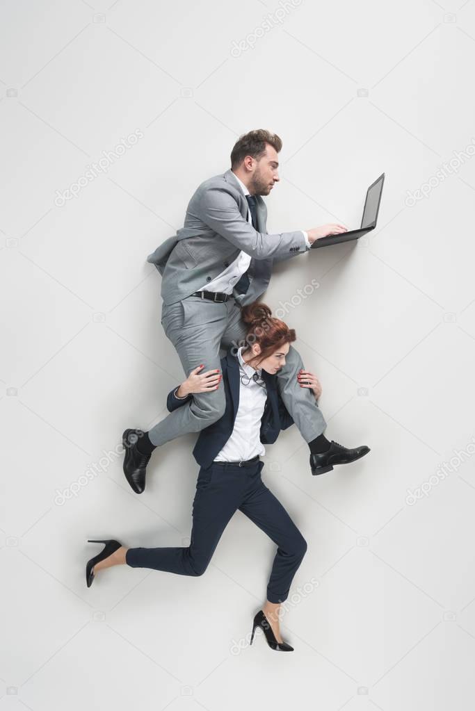 overhead view of businesswoman carrying businessman that working on laptop isolated on grey