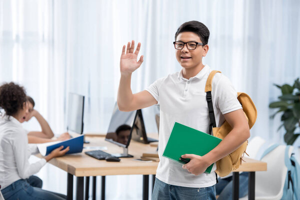 young asian student boy waving hand in classroom with friends