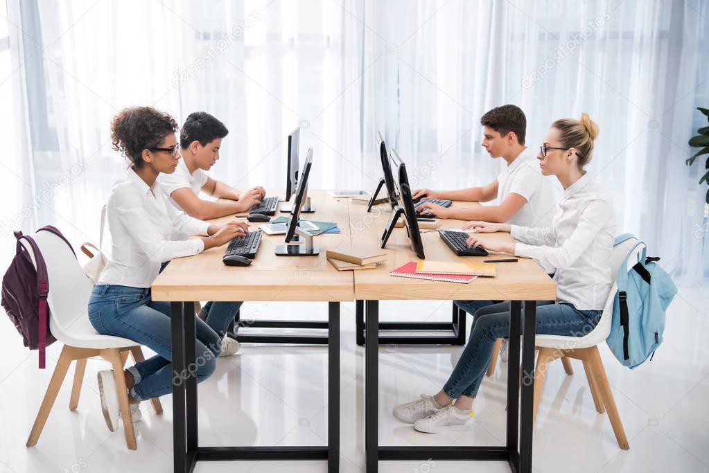 side view of four young multicultural students studying on computers 