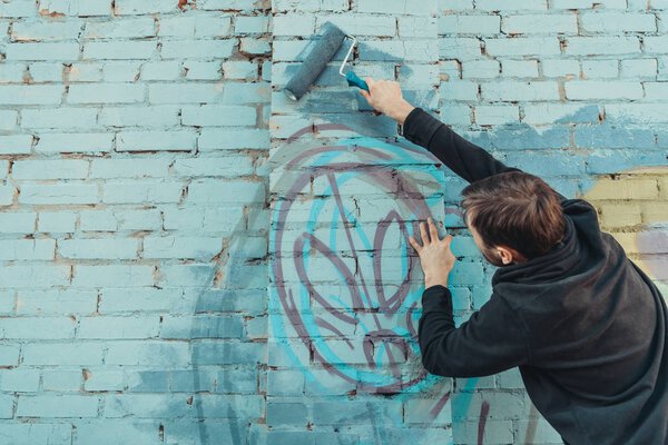 male street artist painting colorful graffiti on wall with roller