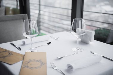 Düzenlenmiş çatal bıçak takımı, boş kadehlerin ve menü görünümünü restoranda beyaz masa örtüsü ile tabloda kapatın