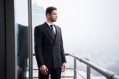 portrait of young pensive man in suit standing at balcony clipart