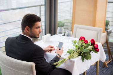 restoranda kız için bekleyen smartphone ile takım elbiseli genç adam
