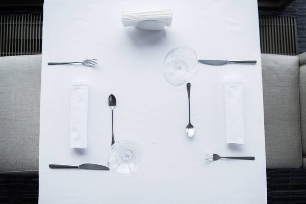 top view of arranged cutlery and wineglasses on table with white tablecloth in restaurant