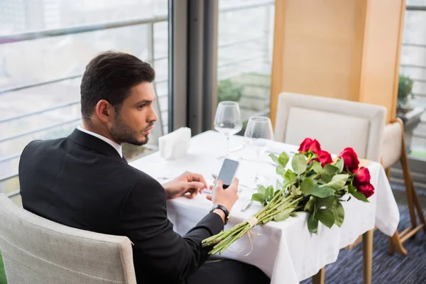 レストランで恋人を待っているスマート フォンでスーツを着た若い男 — ストック写真