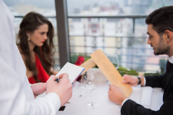selective focus of waiter writing down visitors order in restaurant