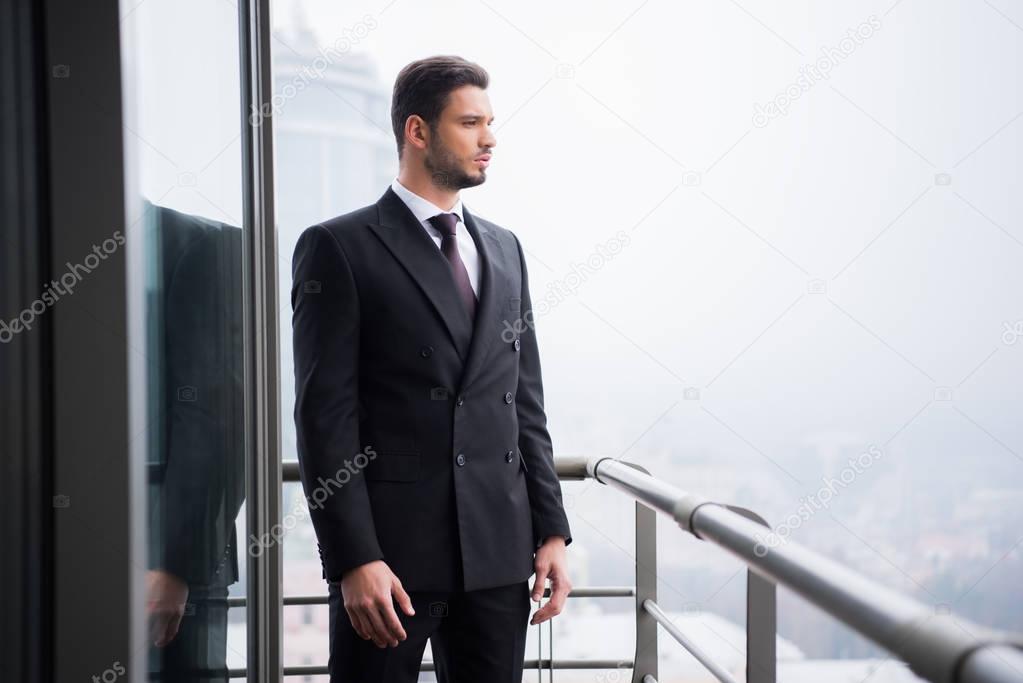 portrait of young pensive man in suit standing at balcony