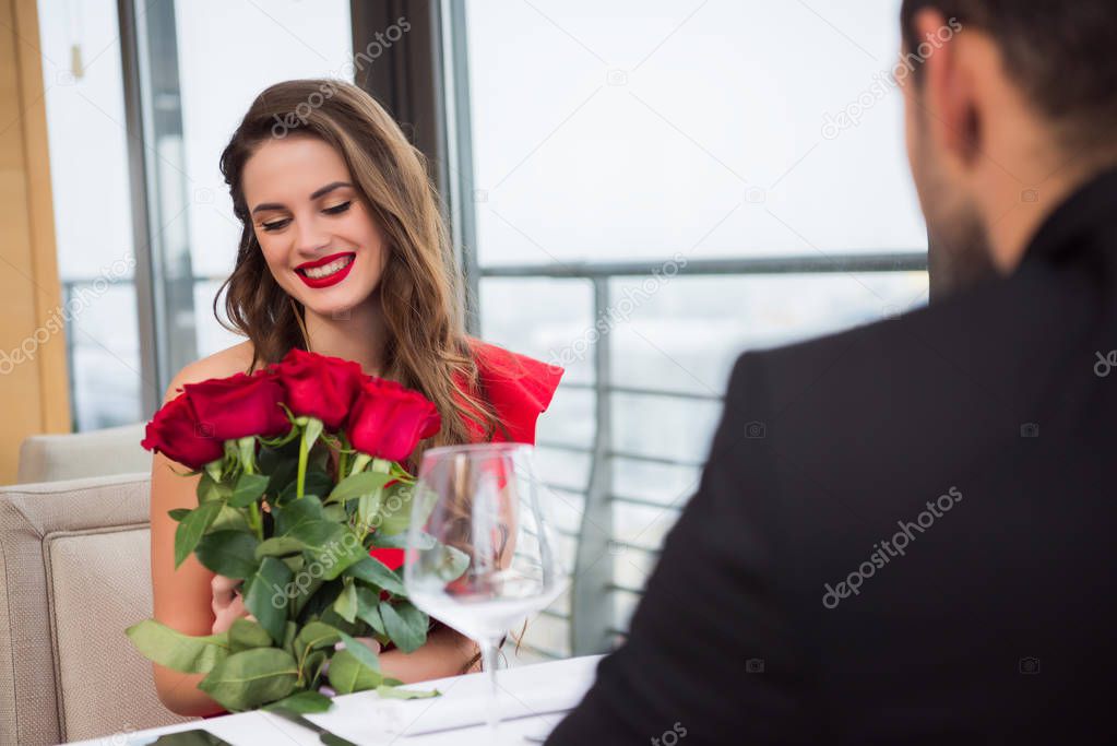 smiling woman with bouquet of roses during romantic date with boyfriend in restaurant, st valentine day