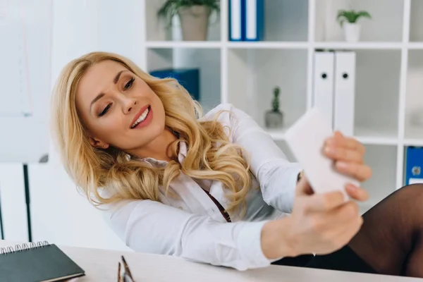 微笑的女商人带着智能手机在工作场所自拍 — 免费的图库照片