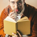 Portrait of young man with cigar and book in hands looking at camera isolated on beige