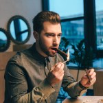 Portrait of young man lighting up cigar while sitting at table in cafe