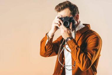obscured view of fashionable man taking picture on photo camera isolated on beige clipart