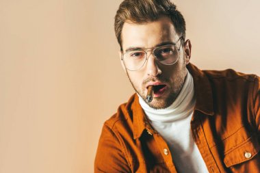 bej üzerinde izole kamera bakarak puro ile şık genç adam portresi