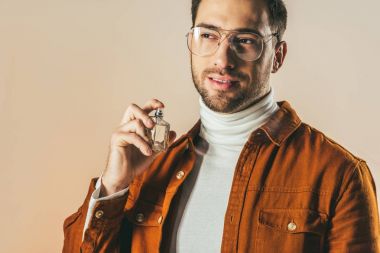 portrait of stylish young man applying perfume isolated on beige clipart