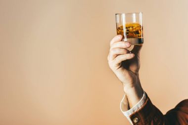 cropped shot of man holding glass of whiskey isolated on beige clipart
