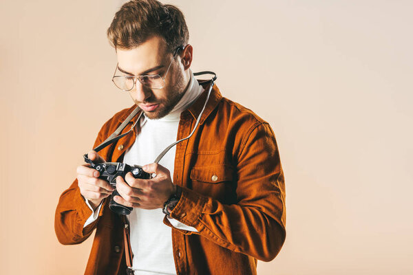 portrait of focused stylish man looking at photo camera in hands isolated on beige