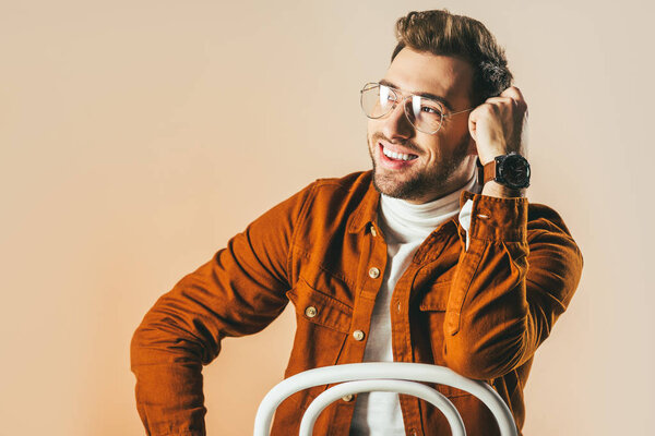 portrait of happy man in fashionable clothing and eyeglasses looking away isolated on beige