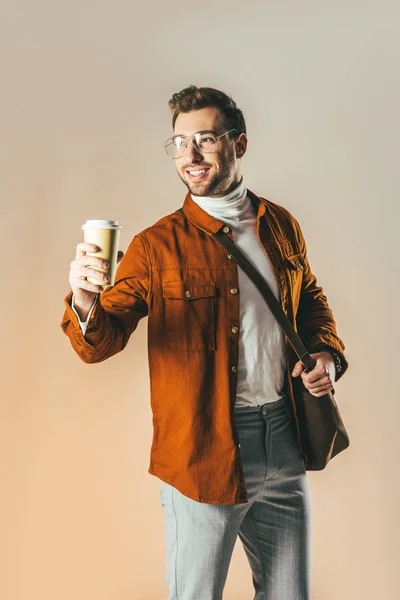 よそ見やコーヒーに手で孤立したベージュの使い捨てカップを示す笑みを浮かべて男の肖像 — ストック写真