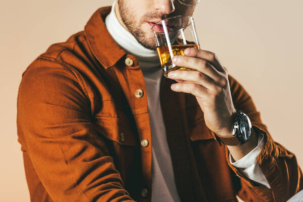 partial view of man in stylish clothing with glass of whiskey in hand isolated on beige