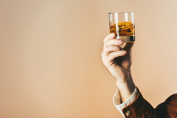 cropped shot of man holding glass of whiskey isolated on beige