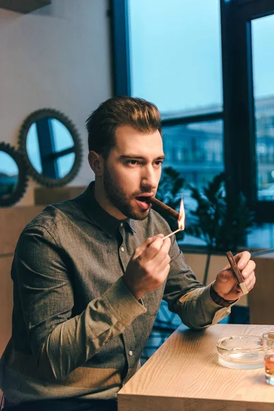 Portrait Young Man Lighting Cigar While Sitting Table Cafe — Free Stock Photo