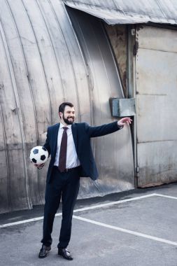 takım elbise uzağa sokakta futbol oynarken işaret içinde genç gülümseyen iş adamı