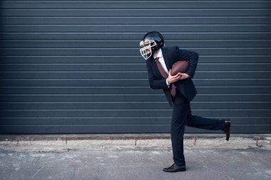 takım elbise ve rugby kask içinde genç işadamı sokakta çalışan eller top ile yan görünüm