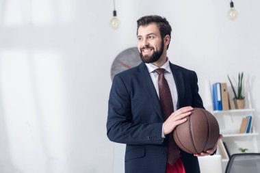 portrait of businessman in jacket holding basketball ball in office clipart