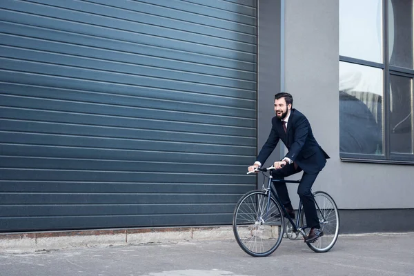 自転車に乗って通りスーツで青年実業家の笑みを浮かべてください — ストック写真