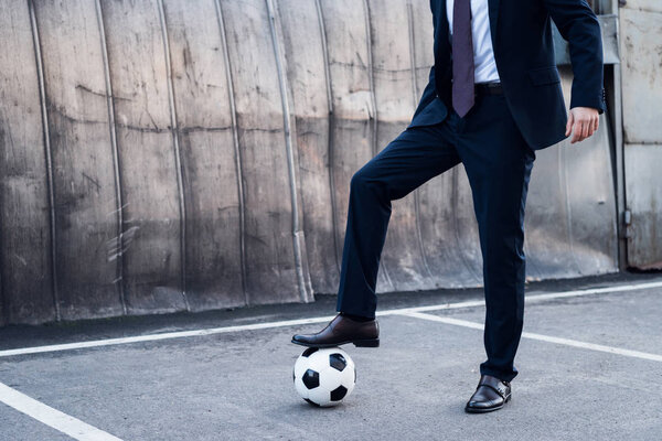 частичный взгляд бизнесмена в костюме, играющего в футбол на улице
