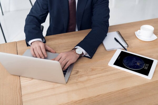 частичный взгляд бизнесмена, работающего на ноутбуке на рабочем месте с планшетом в офисе
