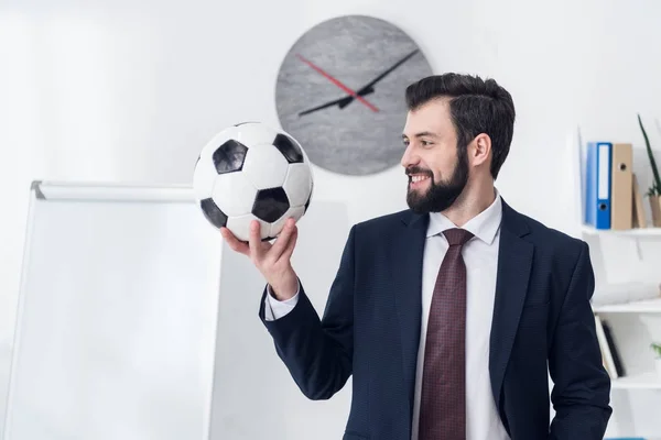 portrait of smiling businessman holding soccer ball in office