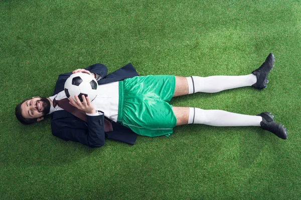 overhead view of businessman with soccer ball resting on green lawn