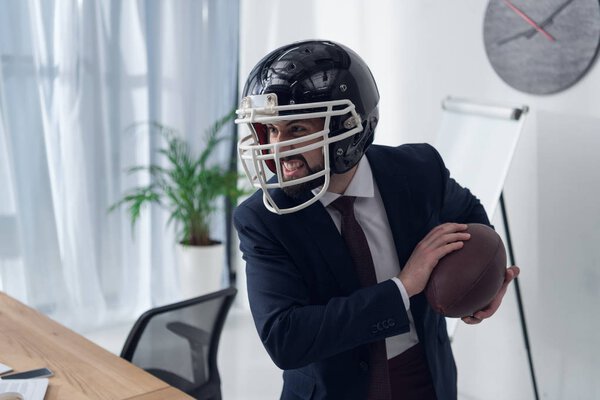 young furious businessman in helmet playing rugby in office