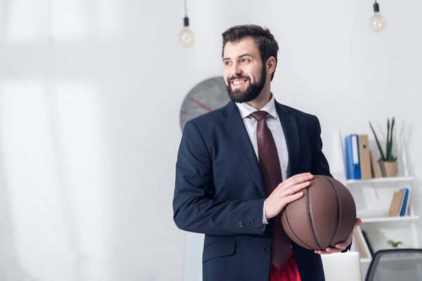portrait of businessman in jacket holding basketball ball in office