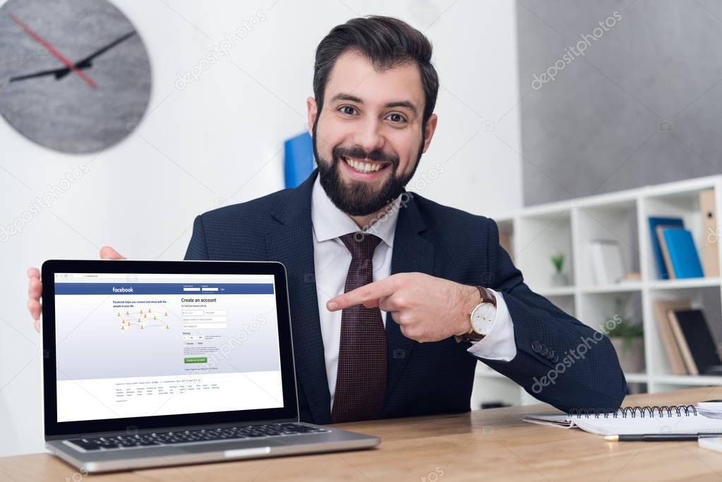 Portrait of smiling businessman pointing at laptop at table in office