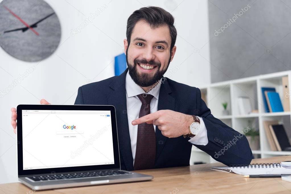 Portrait of smiling businessman pointing at laptop at workplace in office