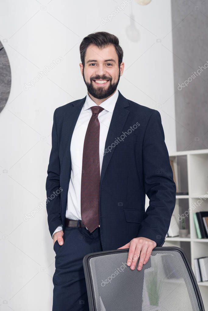 portrait of cheerful businessman in suit standing at workplace in office