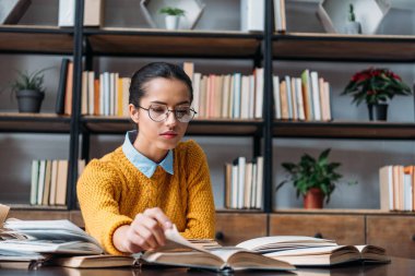 young student girl preparing for exam at library and reading book clipart