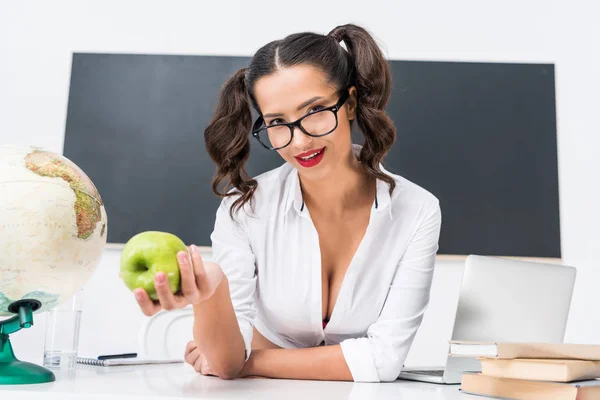 young sexy teacher with green apple sitting at workplace in class