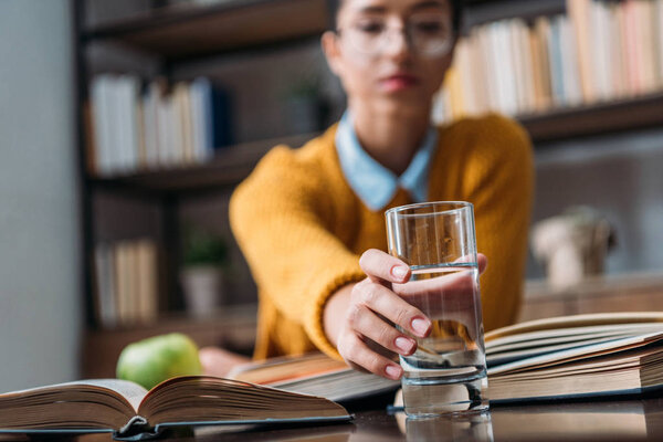 young student girl preparing for exam at library and reaching for glass of water