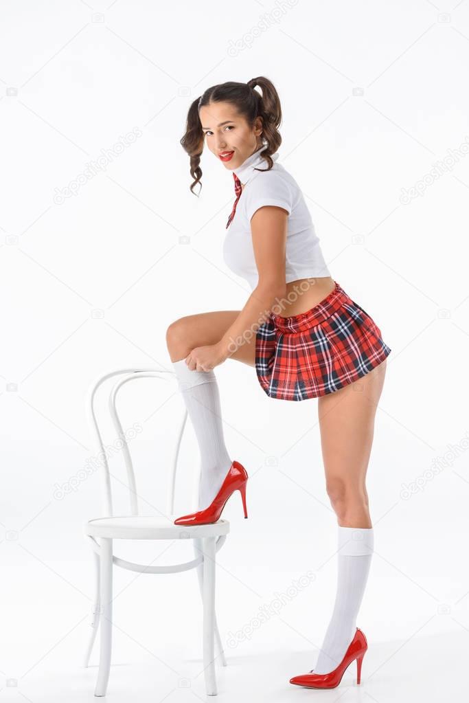 young sexy schoolgirl putting on stockings while standing on chair isolated on white