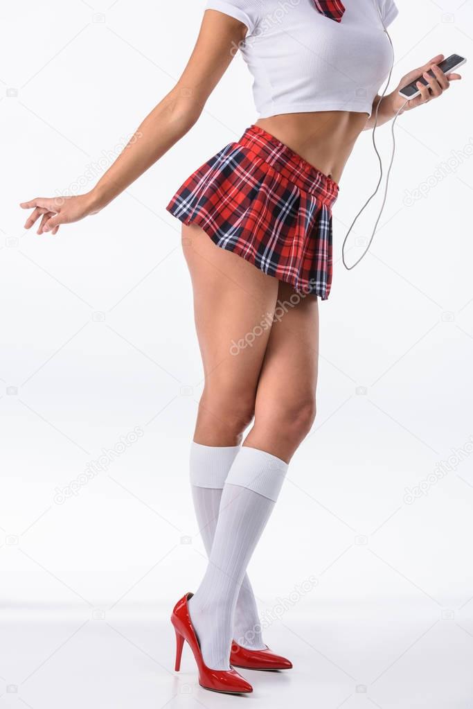 cropped shot of sexy schoolgirl listening music with headphones and smartphone isolated on white